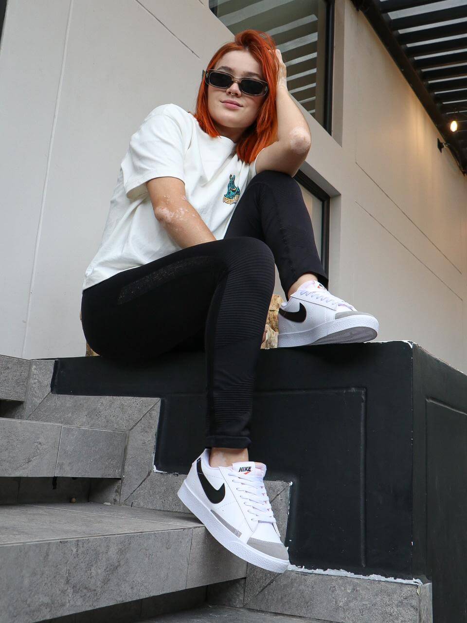 Mujer con tenis Nike Blazer en estilo retro, sentada en escalones urbanos, demostrando versatilidad y moda urbana.